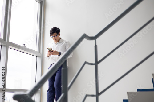 Handsome office worker hold mobile phone in hand chat with girlfriend by mobile phone at modren office balcony in relax time.
