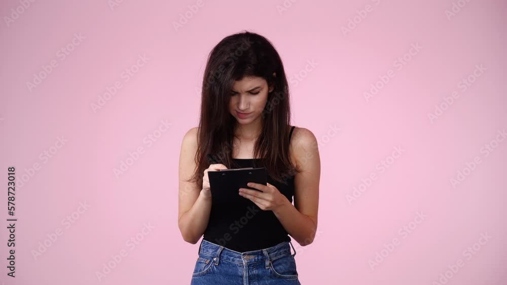 4k video of one girl which thinks and notes something with a pen on tablet over pink background. 4k video of one girl which thinks and notes something with a pen on tablet over pink background.