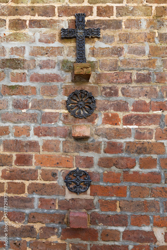 Vertical view of old wrought iron decorative cross and anti-earthquake and hurricane rod gib plates on brick wall, Charleston, SC, USA