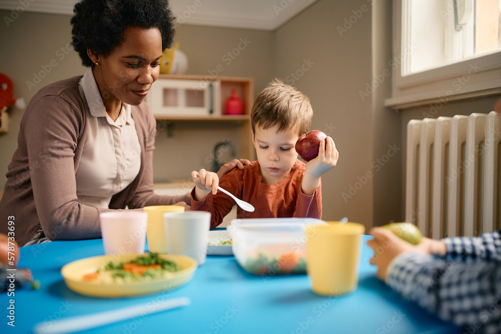 Smiling black female teacher and little boy during lunch at kindergarten. Smiling black female teacher and little boy during lunch at kindergarten.