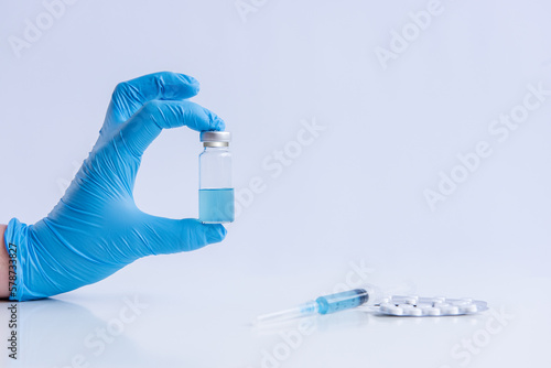 On white isolated background, hands of doctor in medical blue gloves hold ampoule vaccine against virus