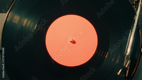 Close-up of a vinyl record with a orange sticker spinning on a retro turntable from top view. Black retro vinyl record on an old player. Close-up of a rotating plate on a player