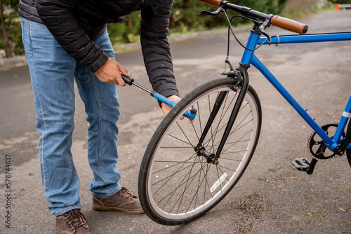 Man fixing a blue fixie bike wearing jeans and a black coat