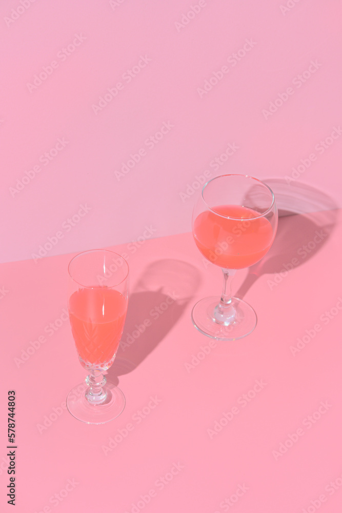 two glasses of wine are sitting on surface with. pink background. still life, aestheticism. minimalism two glasses of wine are sitting on surface with. pink background. still life, aestheticism. minimalism