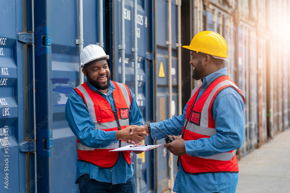 Portrait of Two African Engineer or foreman wears PPE shaking hand with cargo container background at sunset. Logistics global import or export shipping industrial concept. Portrait of Two African Engineer or foreman wears PPE shaking hand with cargo container background at sunset. Logistics global import or export shipping industrial concept.