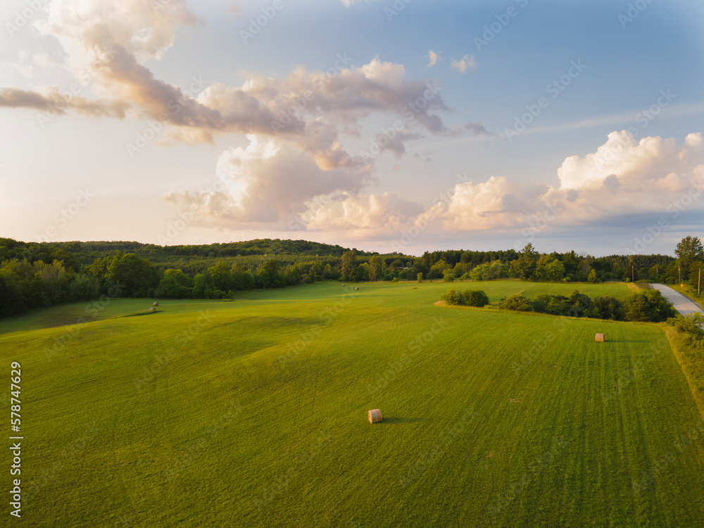 Aerial landscape panorama with hay bales at freshly mown vast field at sunset hour. Sunny day, blue sky, soft light. Farming, agriculture, harvest, pasture, livestock concept. Aerial landscape panorama with hay bales at freshly mown vast field at sunset hour. Sunny day, blue sky, soft light. Farming, agriculture, harvest, pasture, livestock concept.