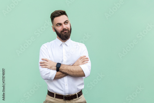 Young adult businessman with folded arms and looking away with smile and dreaming expression.