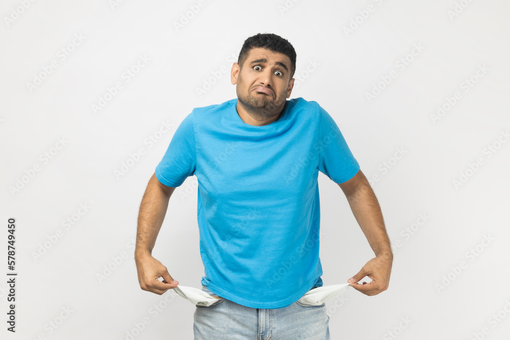Sad poor attractive man in T- shirt standing showing his empty pockets, has no money, lost his job. Sad poor attractive man in T- shirt standing showing his empty pockets, has no money, lost his job.