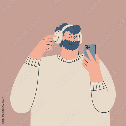 Cute young man in over-ear headphones on his head and with a smartphone in his hand. Bearded guy. Character is listening to music, an audiobook, or a podcast. Vector isolated illustration for design.