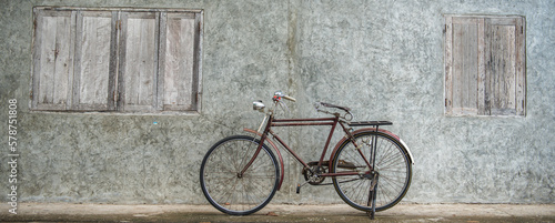Banner panorama size of Vintage bicycle on old rustic dirty wall house, many stain on wood wall. Classic bike bicycle on decay brick wall retro style. Cement loft partition and window background. © BESTIMAGE