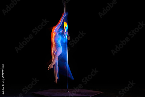 Femininity and sensuality. Young girl performing pole dance isolated over black studio background with mixed neon lights. Concept of sport and dance, beauty of movements, action, modern style