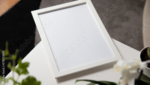 Blank photo frame to place text or image, on white wooden background with flowers around photo