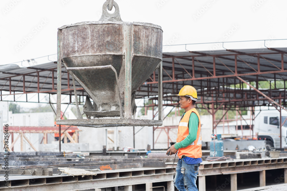 Construction workers control and moving wet concrete by concrete bucket for building precast concrete wall at construction site