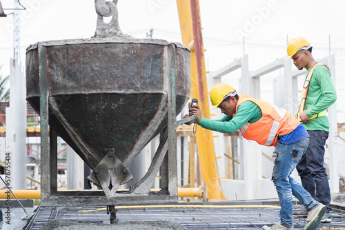 Construction workers pouring wet concrete by concrete bucket for building precast concrete wall at construction site photo