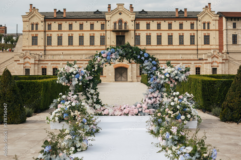 A round arch for the painting of the newlyweds decorated with greenery, blue, pink and white flowers against the backdrop of the castle. Wedding outdoor concept 