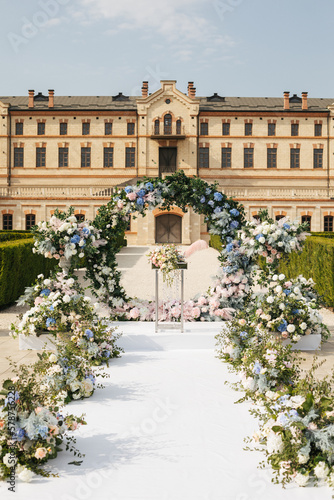 A round arch for the painting of the newlyweds decorated with greenery, blue, pink and white flowers against the backdrop of the castle. Wedding outdoor concept 