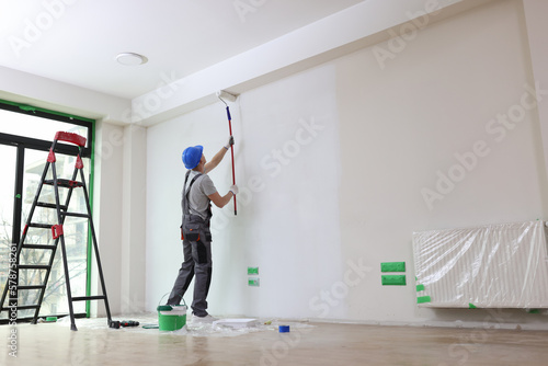 Male painter paints house wall with roller brush. photo