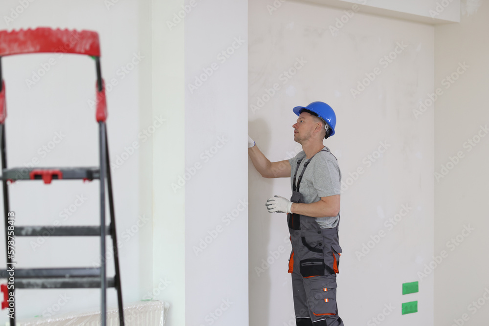 Repairman in hard hat checks problem in wall of house. Repairman in hard hat checks problem in wall of house.