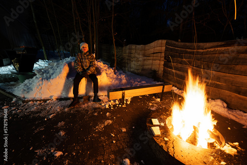 Boy sit by the fire pit in winter night.