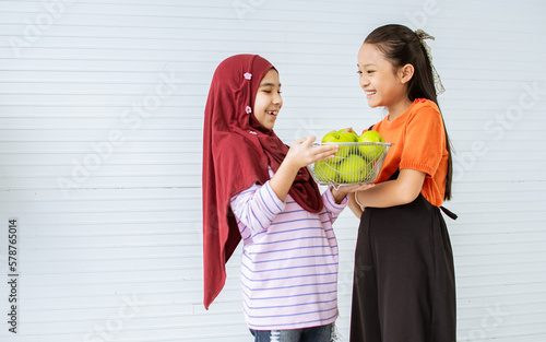 Two teenage diverse girls wearing casual clothes, standing in indoor home, sharing green apples, eating together for good health, smiling with happiness, healthy. Education, Friend Concept. photo