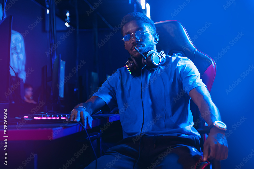 Portrait young American African man professional gamer of online video game with headphones, neon background in computer club - obrazy, fototapety, plakaty 