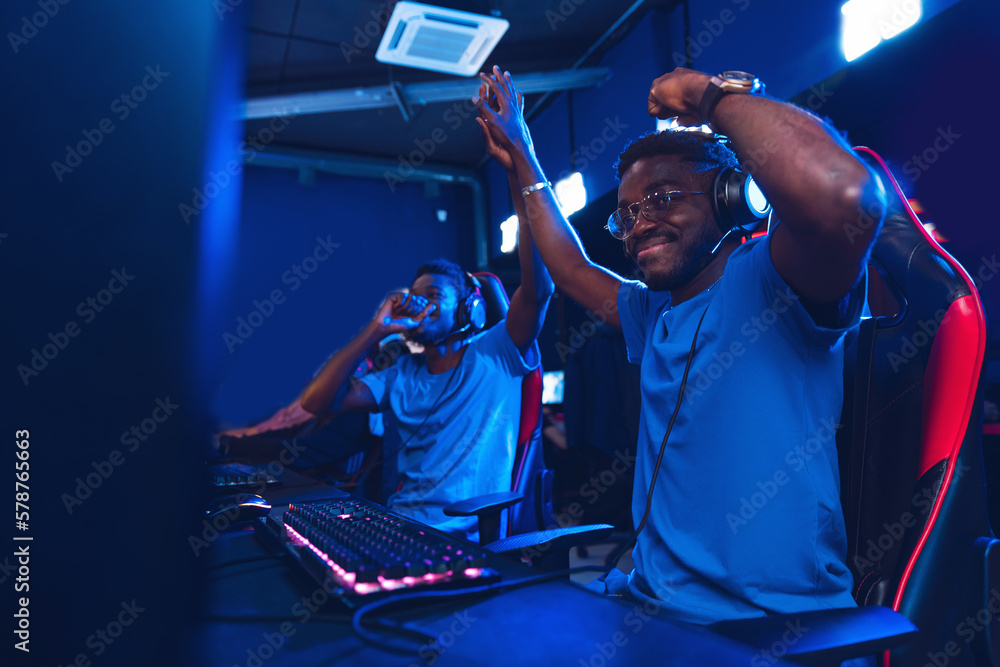 African Streamers young mans rejoices in victory professional gamer playing online games computer with headphones, neon color - obrazy, fototapety, plakaty 