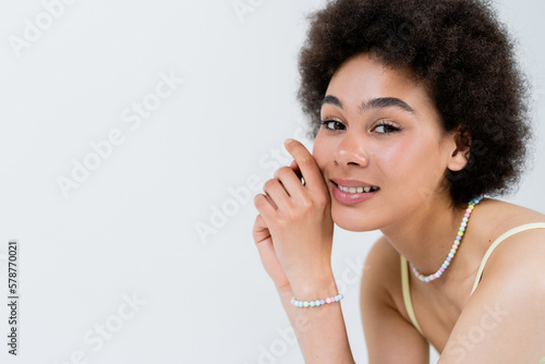 Portrait of smiling african american woman in necklace and colorful bracelet isolated on grey.