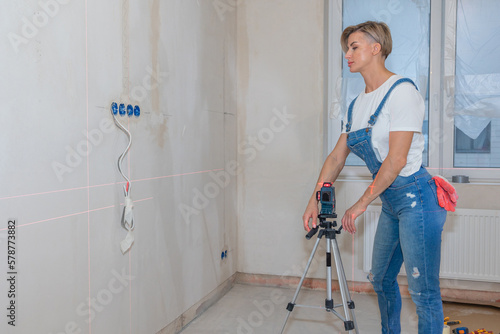 Woman makes repairs in new apartment. Builder levels walls using laser level. High quality photo