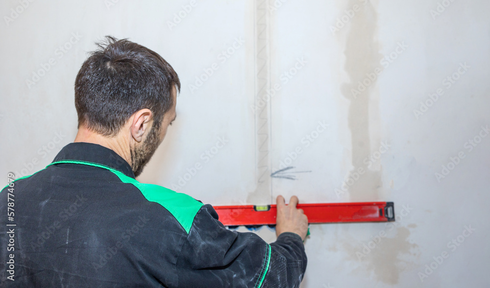 Renovation at home. Man makes repairs in new apartment. Worker levels walls with building water level, measurement tool. High quality photo