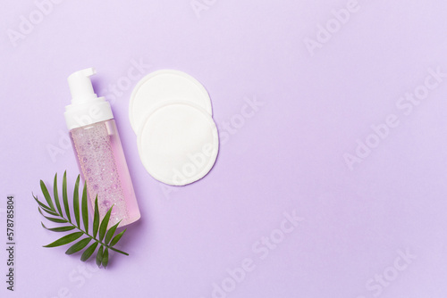 Foaming facial cleanser and with eco pads on color background, top view