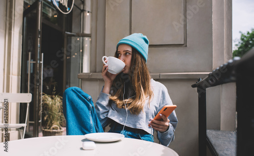 Fotografie Young millennial female using application on mobile phone while drink coffee