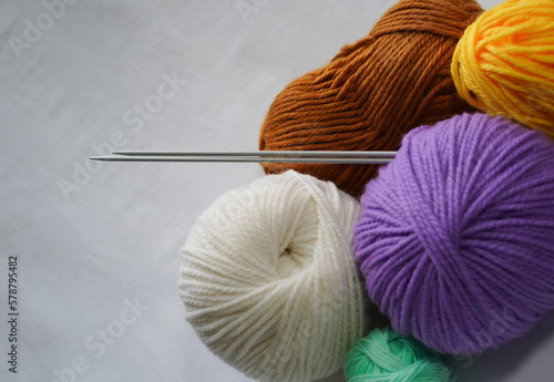 Knitting needles and skeins of yarn on white background. Multicolored balls of acrylic and woolen yarn with knitting needles sticking out of them, as if rolling down the wall. Close-up, copy space.