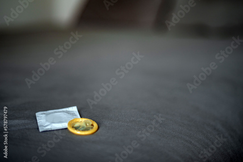 Detalle de dos preservativos, uno con envoltorio y otro sin él sobre una cama con sábanas grises. Sexo seguro. Protección contra embarazos y enfermedades de transmisión sexual. Métodos anticonceptivos