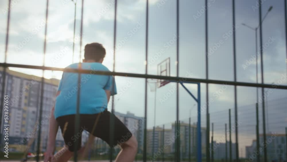 Young Man Practicing Basketball at Sunset on Court with Cinematic Back View in Residential Area Young Man Practicing Basketball at Sunset on Court with Cinematic Back View in Residential Area