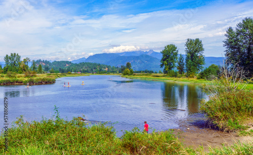 Canoeists and paddleboarders making their way up Pitt River, BC, Canada during summer, with scenic mountain backdrop.
