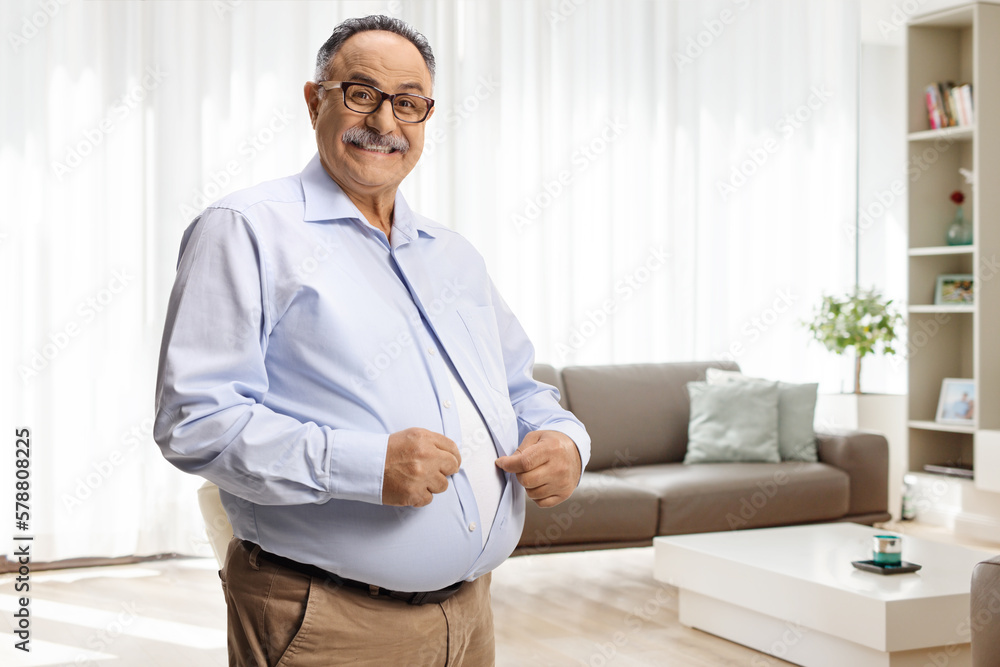 Mature man with big belly buttoning a shirt in a living room
