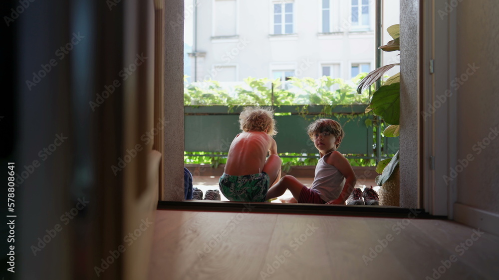 Children sitting by door step putting shoes on outside. Older brother helping younger sibling to put shoe by doorstep Children sitting by door step putting shoes on outside. Older brother helping younger sibling to put shoe by doorstep
