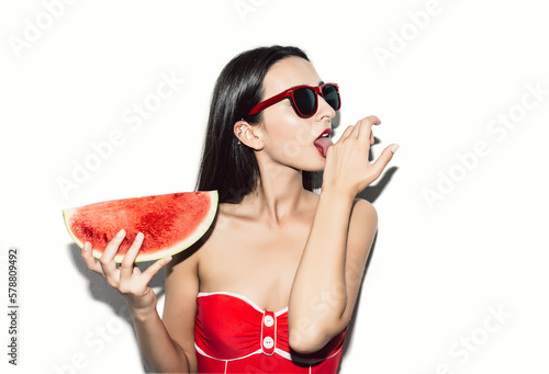 Flash style close up portrait of sexy brunette girl with red lips and sunglasses with red watermelon licking her hand like a cat with tongue on white background. Vacation. Summer travel. 