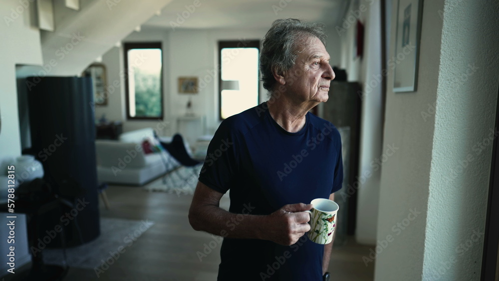 A contemplative mature man stands at home drinking cup of coffee or tea at living room. Portrait of a pensive senior male person in 70s A contemplative mature man stands at home drinking cup of coffee or tea at living room. Portrait of a pensive senior male person in 70s