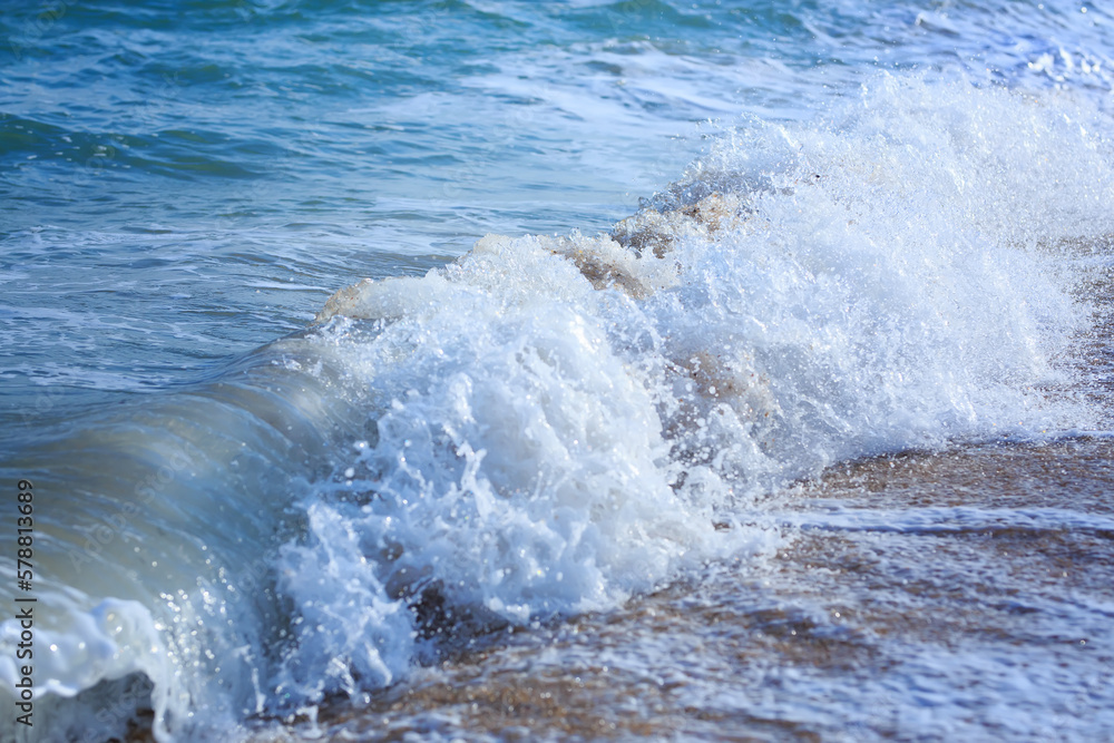 Fototapeta premium Ocean waves crashing on sandy beach. Sea waves breaking on shore. Nature splash on summer day. Sea wave crashing on beach. Splashing sea water with foam.
