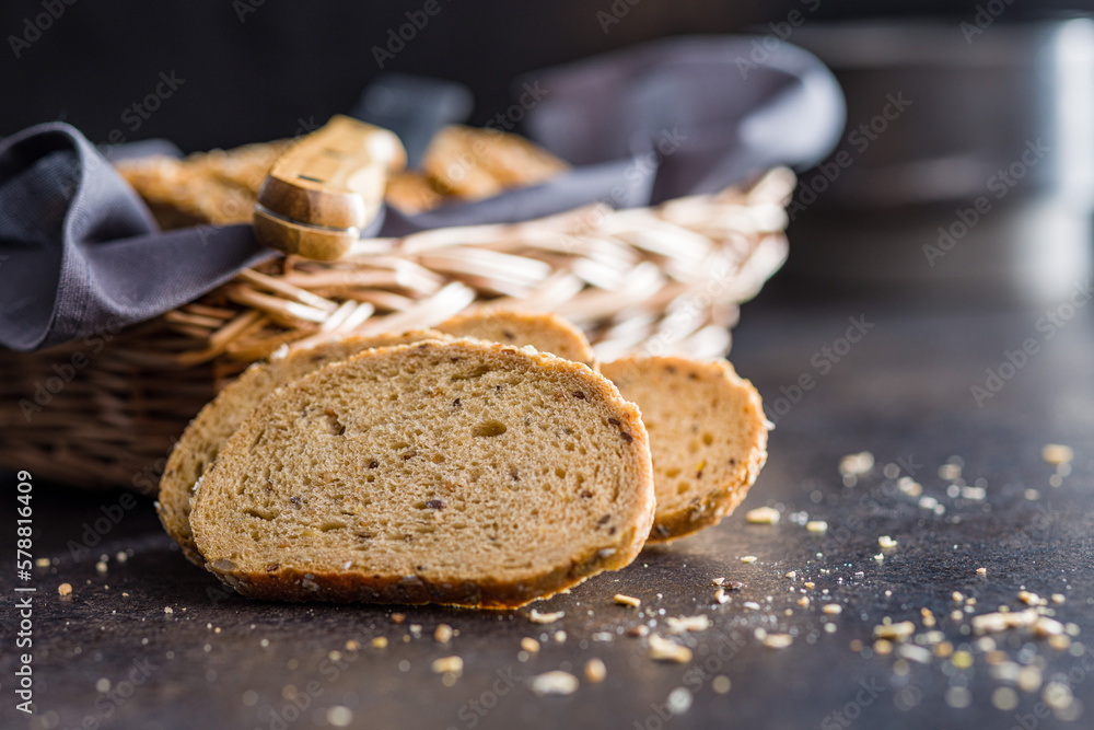 Naklejka premium Sliced whole grain bread. Tasty wholegrain pastry with seeds on black table.