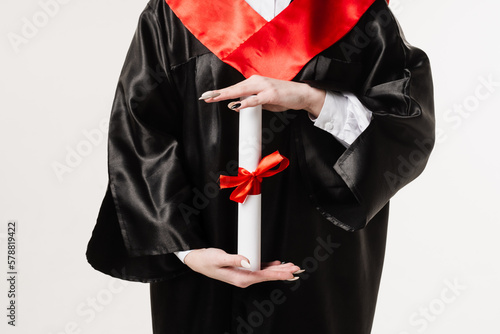 Masters degree diploma in hands close-up. Student in black graduation gown is holding diploma on white background. Graduate girl is graduating high school and celebrating academic achievement.