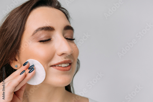 young dark-haired girl removes makeup from her face with a cotton pad, copy space