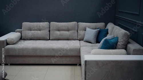 Large, modern, beige sofa with ten beige and blue decorative pillows, next to a dark blue wall.