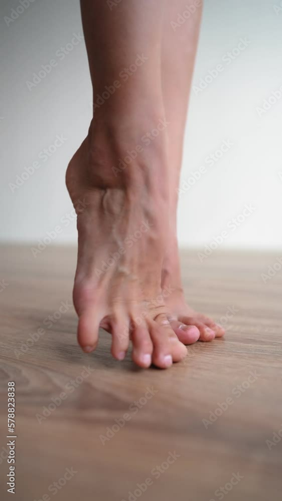 Vertical Video, Beautiful Slim Female Legs Stand on the Parquet Floor on Background of a White Wall and Move Gracefully Barefoot. Concept of Care for the Woman Body and Feet. Slow Motion, Close-up. Vertical Video, Beautiful Slim Female Legs Stand on the Parquet Floor on Background of a White Wall and Move Gracefully Barefoot. Concept of Care for the Woman Body and Feet. Slow Motion, Close-up.