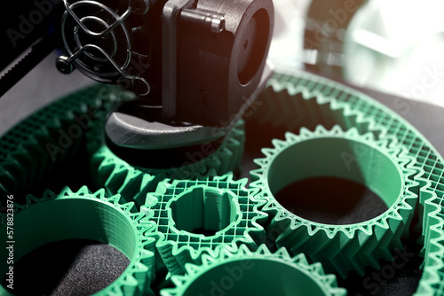 Detail view on print head of 3D-printer making a planetary gear part from mint coloured plastic. selective focus. Visible infill structure and layers at printed part. Modern production concept
