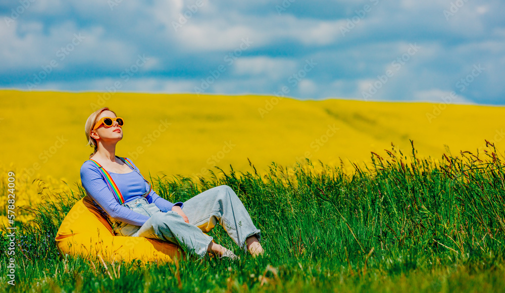 Beautiful female in rainbow LGBT suspenders for pants sitting in bean chair in rapeseed field Beautiful female in rainbow LGBT suspenders for pants sitting in bean chair in rapeseed field