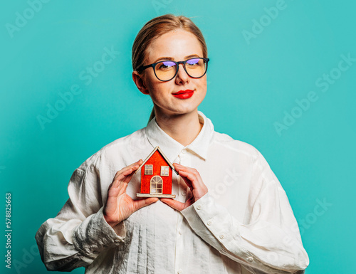 Portrait of beautiful blonde in white shirt with little house on blue background © Masson