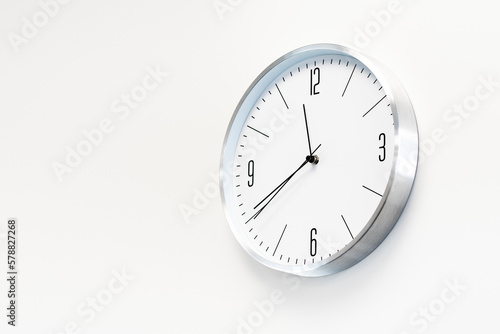 Stylish, round, white clock hangs on a white wall. Place for text, copy space.