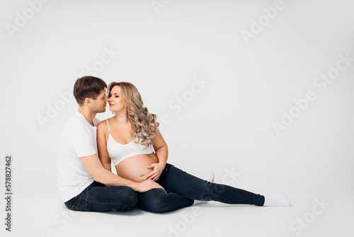 a couple waiting for a child sit on the floor of a cyclorama in a photo studio 